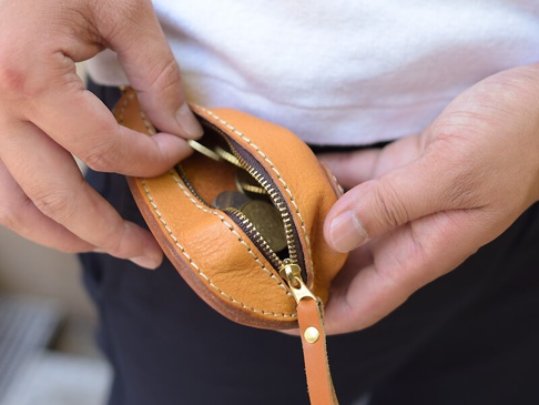 職人手作皮革餃子造型零錢包，淺棕色牛皮材質，銀色拉鍊，附有皮革拉帶。