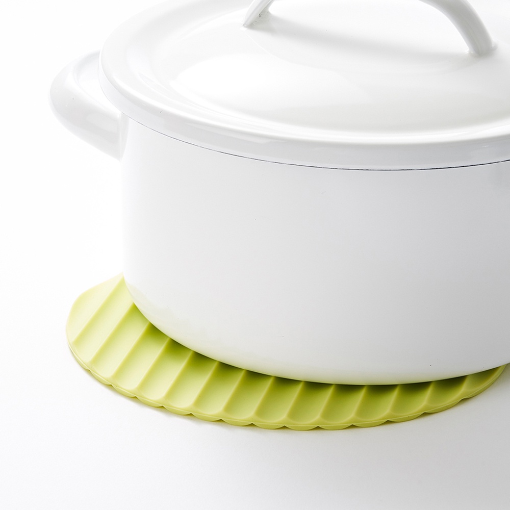 圓形淺綠色矽膠隔熱墊，表面有規則的紋路，用於放置白色鍋具。