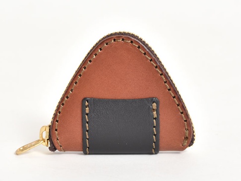 職人手作皮革零錢包，呈現三角形飯糰造型，主體為棕色麂皮，飾有黑色皮革小方塊，並以手工縫線及金色拉鍊裝飾。