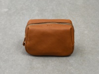 一個棕褐色的皮革拉鍊收納包，表面有「Organ」字樣壓印，拉鍊為金色，包體呈方塊狀，有圓潤邊緣，背景為灰色紋理表面。