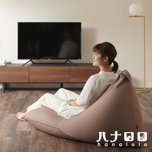 一位女性坐在咖啡色針織布懶骨頭沙發上，沙發呈三角形，旁邊有電視和落地燈。