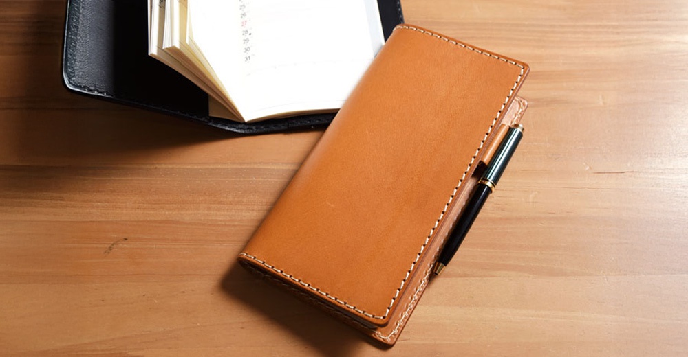 職人手作淺棕色皮革輕便記事本書套，內有筆記本，書套側邊夾有一支黑色筆。