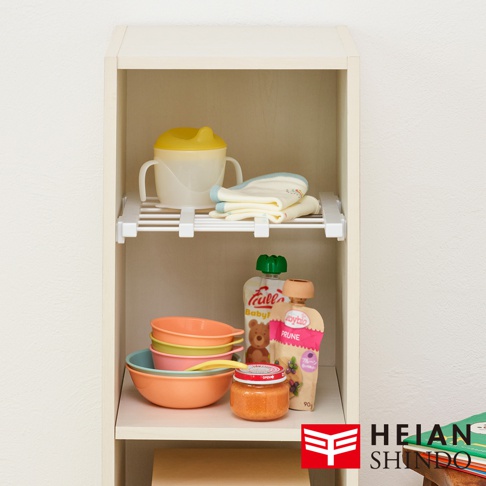 層架上擺放著嬰兒學習杯、疊放的衣物、幾罐嬰幼兒食品和幾個彩色碗。