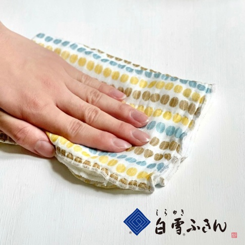 一隻手放在一塊印有圓點圖案（黃色、藍色、棕色）的白色棉質拭巾上，拭巾邊緣有細緻的荷葉邊。