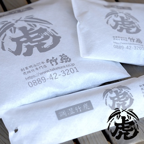 白色包裝的孟宗竹炭產品，印有灰色虎頭與日文「竹虎」圖案，下方標示公司名稱、網址及電話。其中一包竹炭為長條形，上面印有「調濕竹炭」字樣。