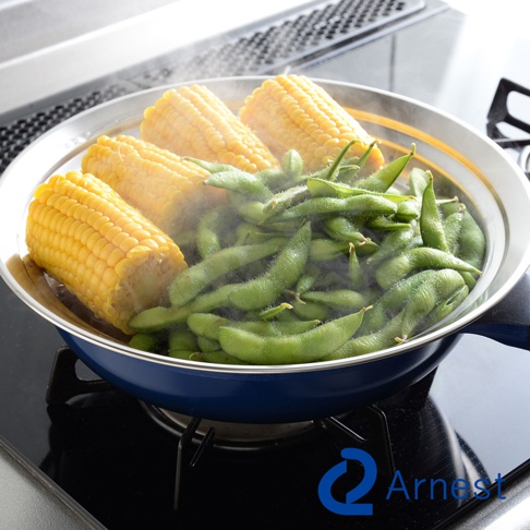 不鏽鋼蒸盤內有玉米段和毛豆，蒸氣冒出。蒸盤置於藍色鍋中，鍋具在爐灶上。