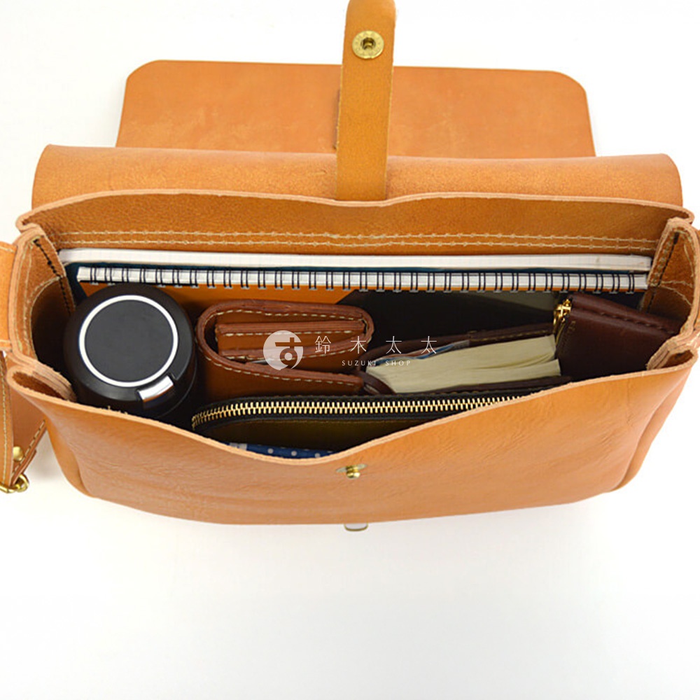 一個棕色皮革包，裡面裝有筆記本、錢包和一個圓形黑盒子。