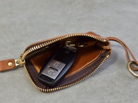 職人手作皮革鑰匙包，棕色，拉鍊開合，內含黑色汽車遙控器，附有皮革繫繩和掛環。