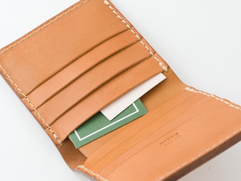 棕褐色皮革製成的二折直式短夾，內部有多個卡槽，其中一個卡槽內插有白色與綠色的卡片。短夾邊緣有米白色的縫線。