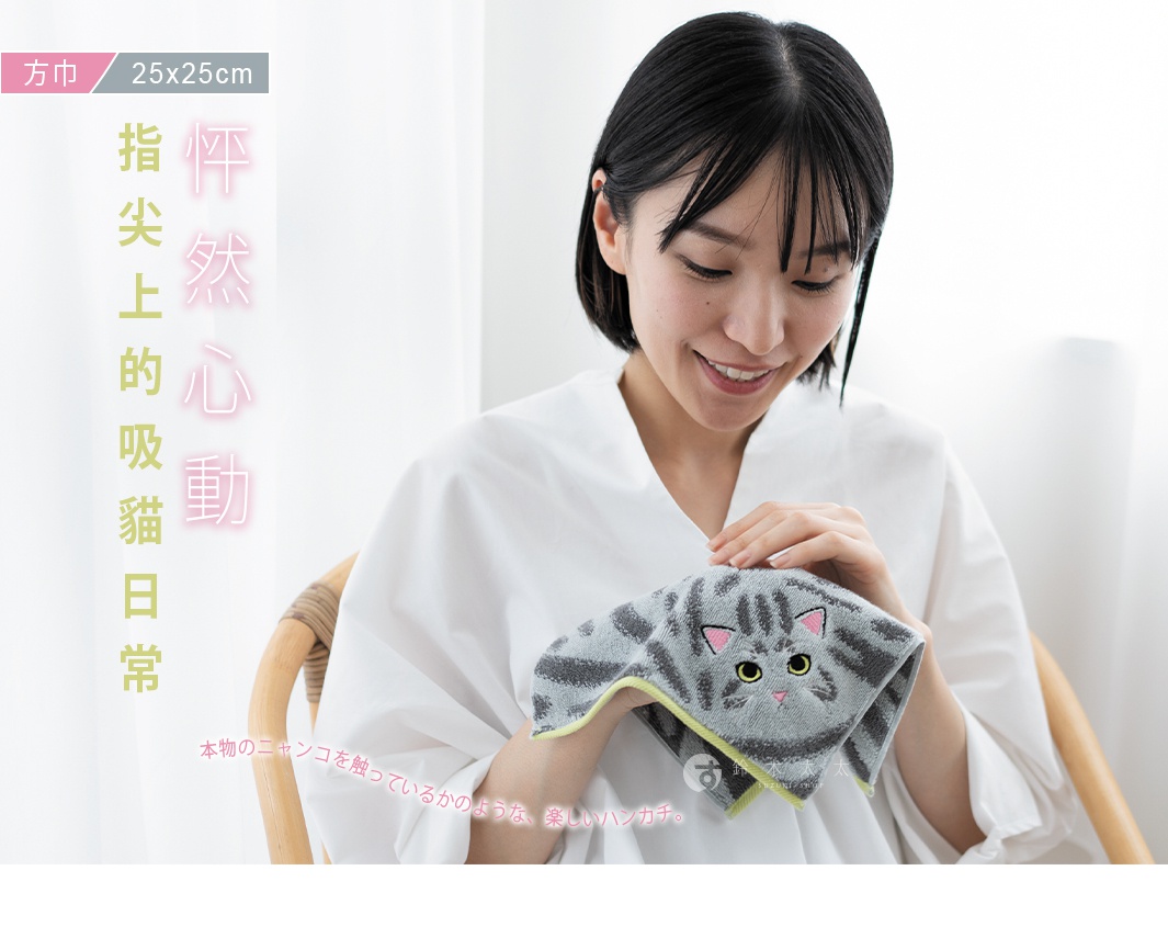 一位留著短髮的女性穿著白色上衣，坐在藤椅上，手中拿著一條灰色虎斑貓造型的方形毛巾，毛巾上繡有精緻的貓咪臉部特徵，圖片左側標示方巾尺寸為二十五乘二十五公分，並配有日文標語，整體氛圍溫馨舒適。