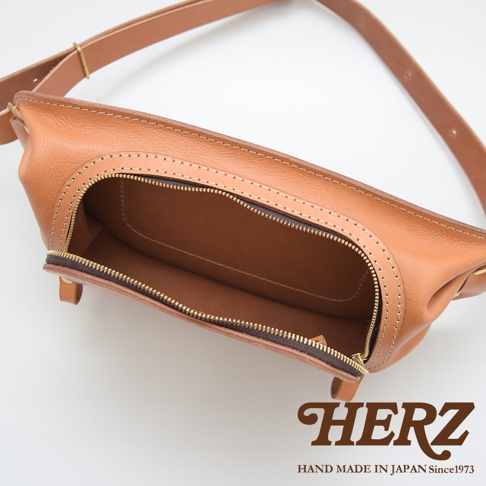 HERZ 職人手作皮革斜背包，展示內部空間和黃銅拉鍊，標有「HAND MADE IN JAPAN Since1973」。