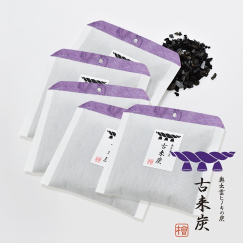 一疊五個白色調濕炭包，頂部邊緣有紫色皺紋紙裝飾，並有打孔。其中一個炭包上印有日文品牌標誌和「古來炭」字樣。旁邊散落著一小堆黑色木炭碎塊。