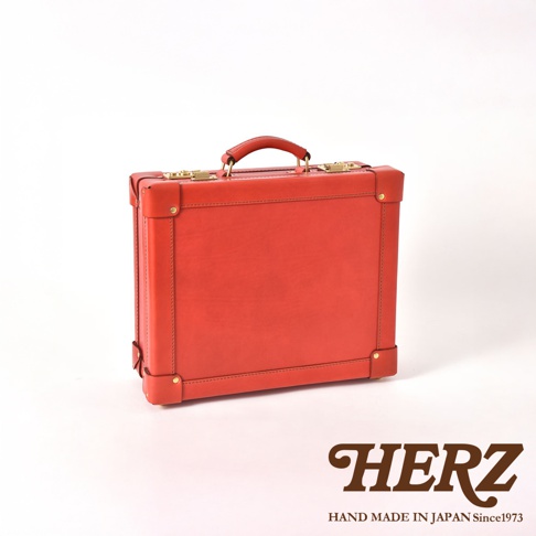 紅色皮革英倫風手提行李箱，帶有金色金屬鎖扣和皮革手柄，箱體邊緣有加固設計。