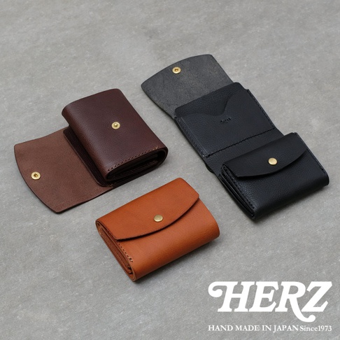 日本HERZ職人手作皮革迷你短夾，展示三種不同顏色的皮革皮夾，包含深棕色、黑色與淺棕色，外觀呈現經典的日式簡約設計，表面帶有細緻的皮革紋理，每個錢包均搭配黃銅質感扣飾，右下角印有HERZ品牌字樣，整體呈現高品質的手工藝質感。