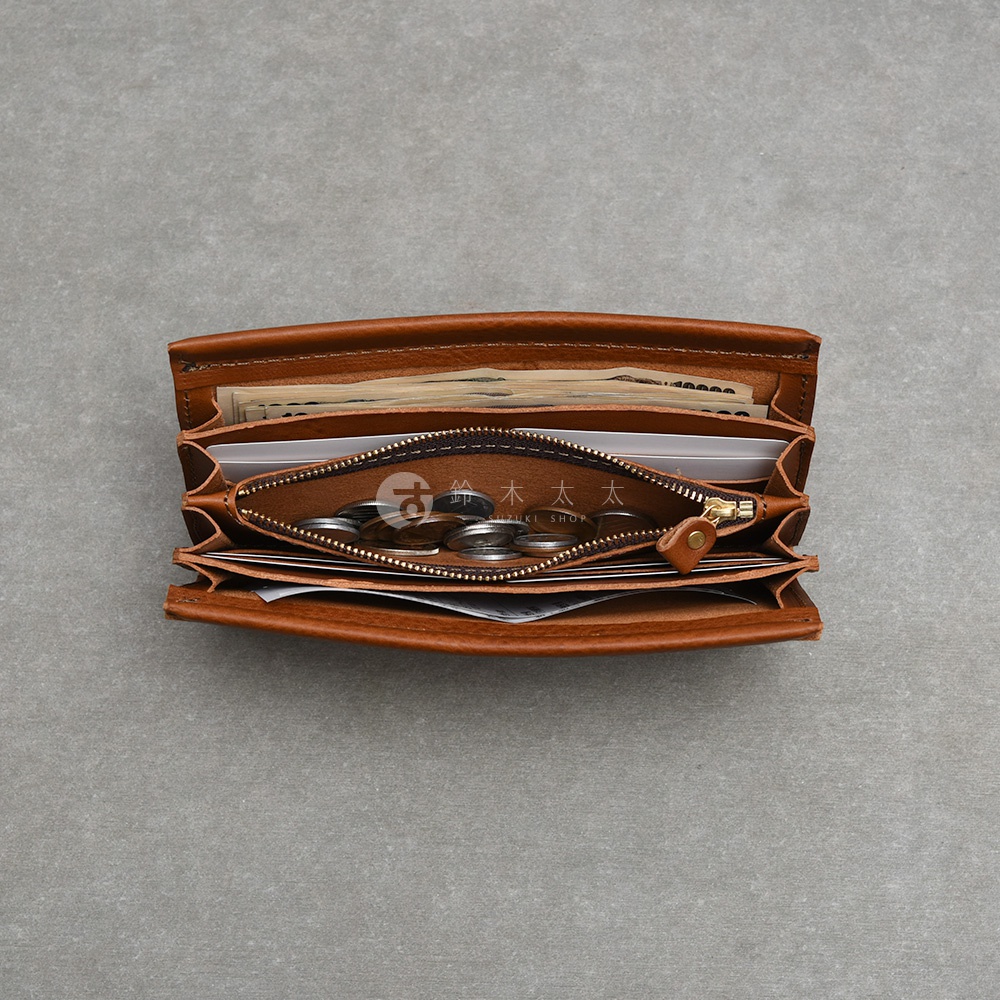 一個由日本HERZ職人手作的棕色皮革長夾，從上方俯視角度拍攝，內部展現了風琴式收納層。錢包中間為拉鍊式零錢袋，並裝有硬幣，兩側夾層則整齊放入了紙鈔與卡片，整體呈現出經典、溫潤的皮革質感與實用的內部構造。