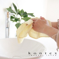 一塊淺黃色的 MOKU LINEN 棉麻拭巾，輕薄且具有吸水性，由雙手拿著，旁邊有水龍頭和洗手盆。