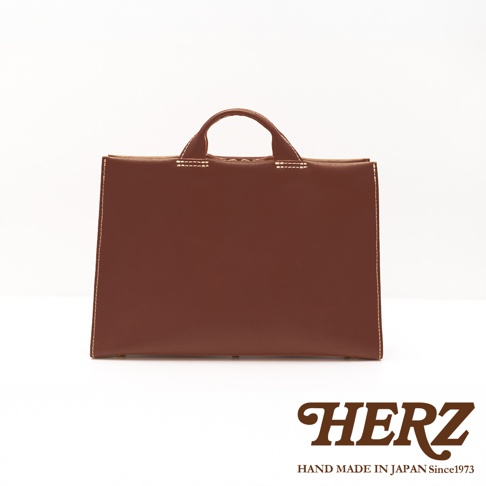 日本HERZ品牌，簡約棕色皮革公事包，有手提把，頂部有縫線裝飾，背景為白色。