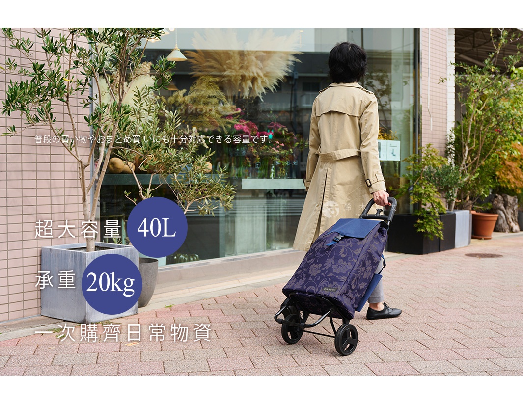 一名女性穿著米黃色風衣，拉著一款深藍色、帶有花紋的輕量折疊大容量購物車，購物車有四個輪子和一個黑色伸縮手柄。