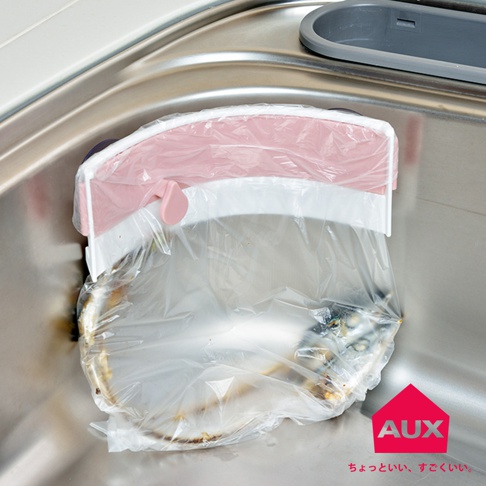 粉色與白色塑膠材質的開合式廚餘架，夾著塑膠袋，掛在不鏽鋼水槽邊緣，塑膠袋內有廚餘。