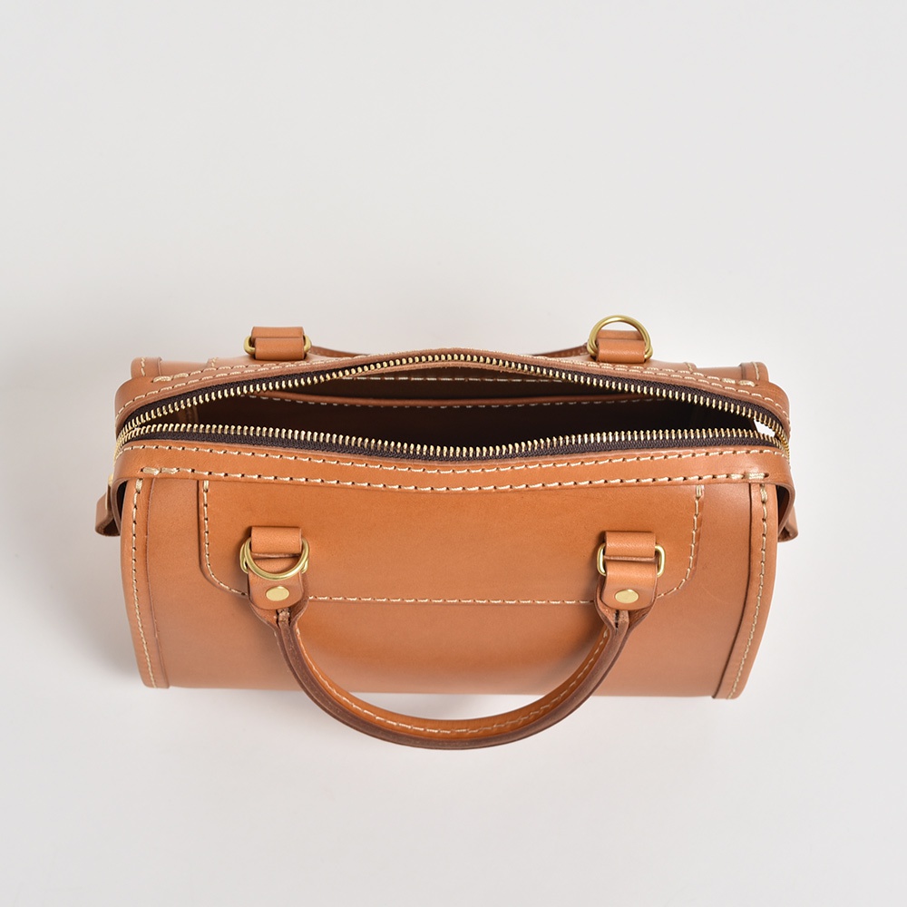 職人手作皮革迷你波士頓包，採用光滑棕色皮革製成，配有黃銅色拉鍊和提把，包身有精緻的白色車縫線裝飾。