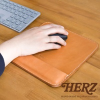 皮革滑鼠墊，棕褐色，手部握著滑鼠，置於滑鼠墊上，旁邊為灰色鍵盤。