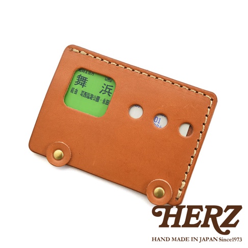 日本HERZ 職人手作皮革交通卡收納夾，外觀像巴士，點綴著金屬鈕扣，並透過縫線手工製作，卡套內可見一張綠色背景的交通票券。