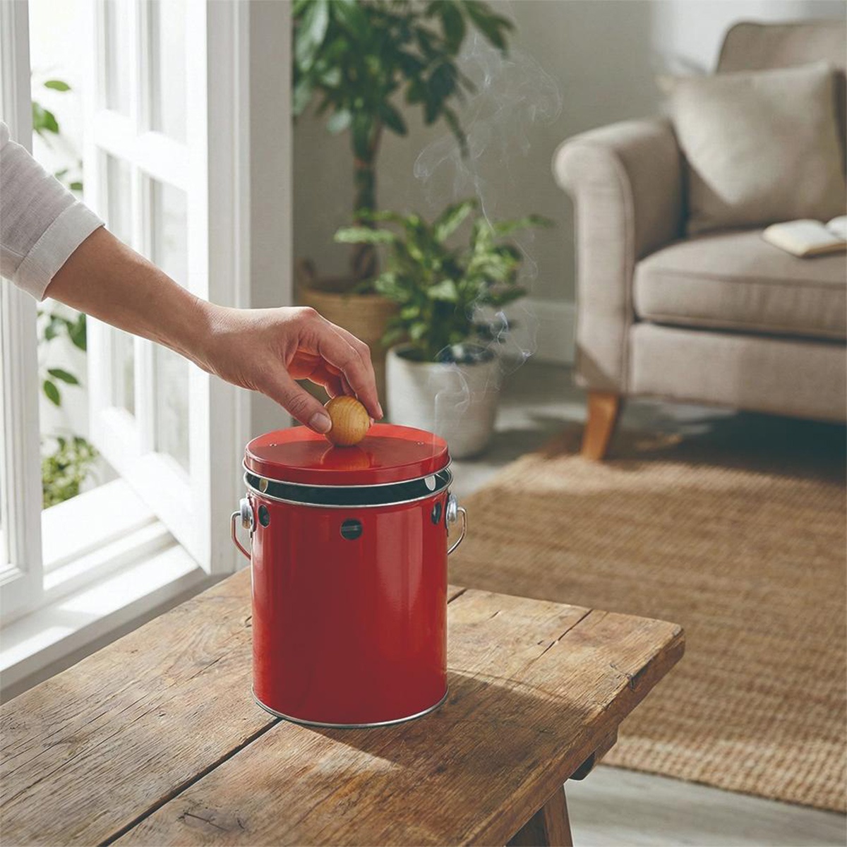 視覺模式： 一個紅色的 OBAKETSU 蚊香桶放在木桌上，煙霧從頂部冒出，一隻手正在將一個小木球放在蓋子上。