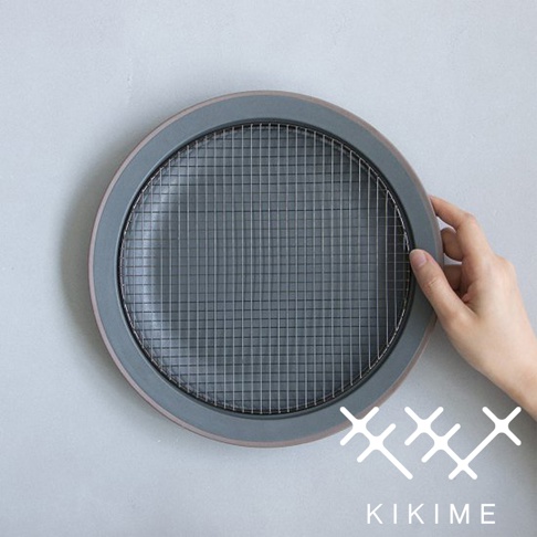 一只手拿著一個灰色陶瓷製的美濃燒瀝油餐盤，盤內嵌有全黑金屬網架。