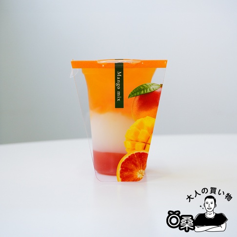 透明杯中盛有三層飲品，從上至下分別為橘黃色、乳白色和粉紅色。杯身側面印有「Mango mix」字樣，以及一顆完整的紅色芒果、切塊的黃色芒果和一片血橙。