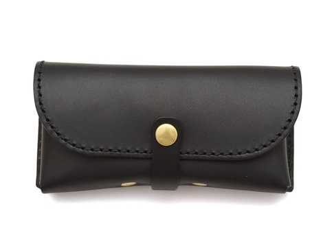 黑色皮革製成的職人手作眼鏡收納盒，附有金色按扣和皮革扣帶，邊緣有縫線裝飾。