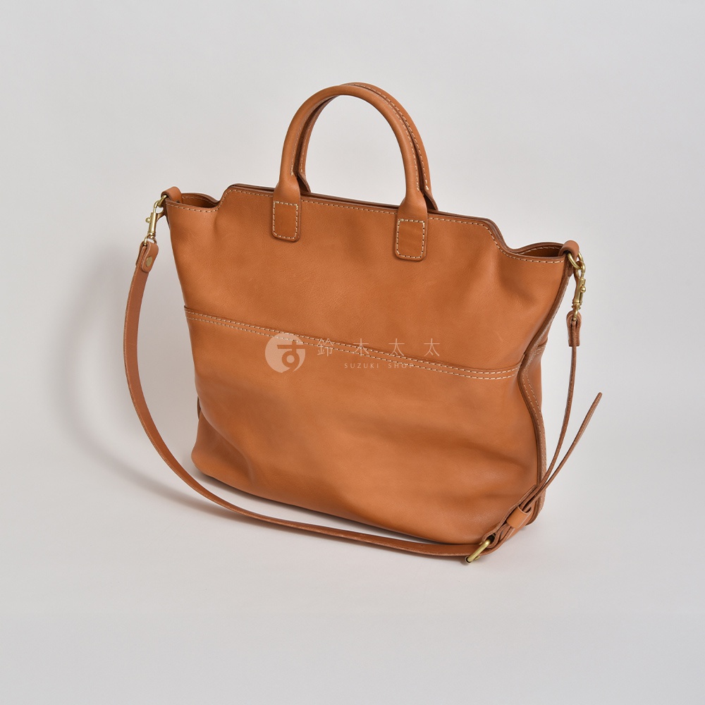 職人手作皮革大容量兩用托特包 T-8，焦糖棕色，天然皮革材質，附有兩條手提把與一條可拆卸斜背帶，包身正面有縫線裝飾，整體風格簡約實用。