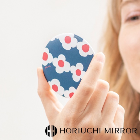 一個藍色圓形口袋小圓鏡，上面印有白色花朵圖案，花心為紅色。鏡面由金屬或塑膠製成，便於攜帶。