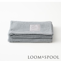 灰藍色純棉大浴巾疊放，上面有淺灰色標籤，下方有 LOOM & SPOOL 商標