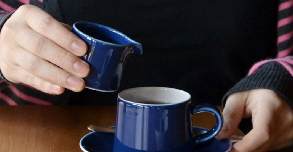 藍色陶瓷M型糖盅，帶有傾倒嘴，由手持著，正要將液體倒入同款藍色馬克杯中。