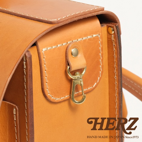 HERZ 品牌標誌，下方印有 HAND MADE IN JAPAN Since1973 字樣，搭配皮革橫式書包的細節特寫，呈現職人手作質感。
