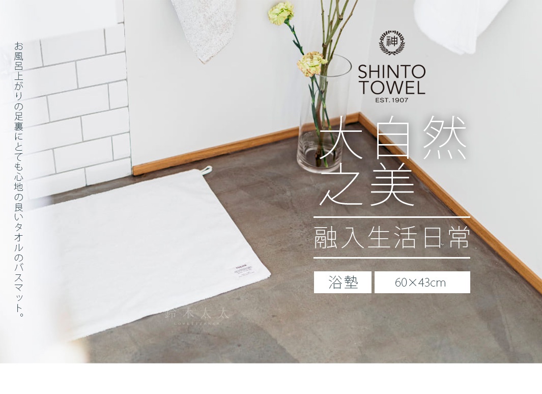 浴室地板上鋪著一張柔軟的白色浴墊，旁邊有花瓶裡插著綠葉和黃色小花，牆上掛著毛巾。