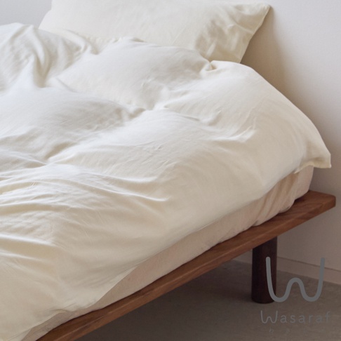 一床純白色雙人被褥，蓋在木製床架上，被褥柔軟蓬鬆，呈現出優雅的褶皺，右下角有Wasaraf的標誌。