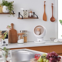 白色的圓形機身，搭配木紋色扇葉的空氣循環扇，擺放在廚房檯面上，旁邊有木質砧板、玻璃罐裝調味料和義大利麵。