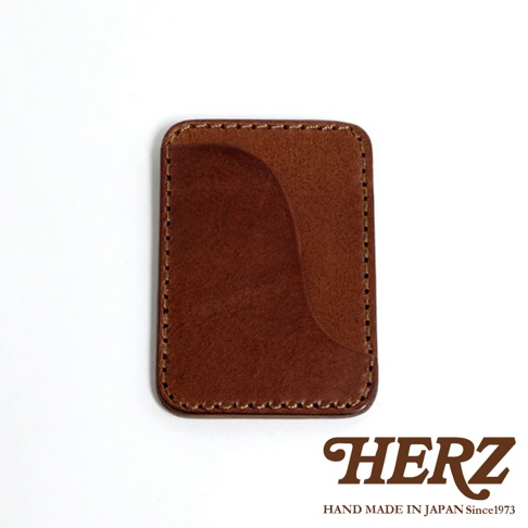 一個紅棕色皮革名片夾，有縫線細節，角落處有HERZ品牌標誌和HAND MADE IN JAPAN Since1973字樣