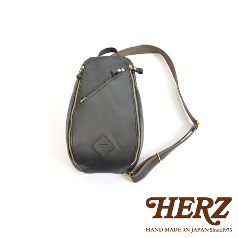 黑色皮革職人手作多功能收納斜背包，正面有斜向拉鍊開口及品牌菱形壓紋，搭配黃銅色拉鍊與可調節式深棕色織帶。