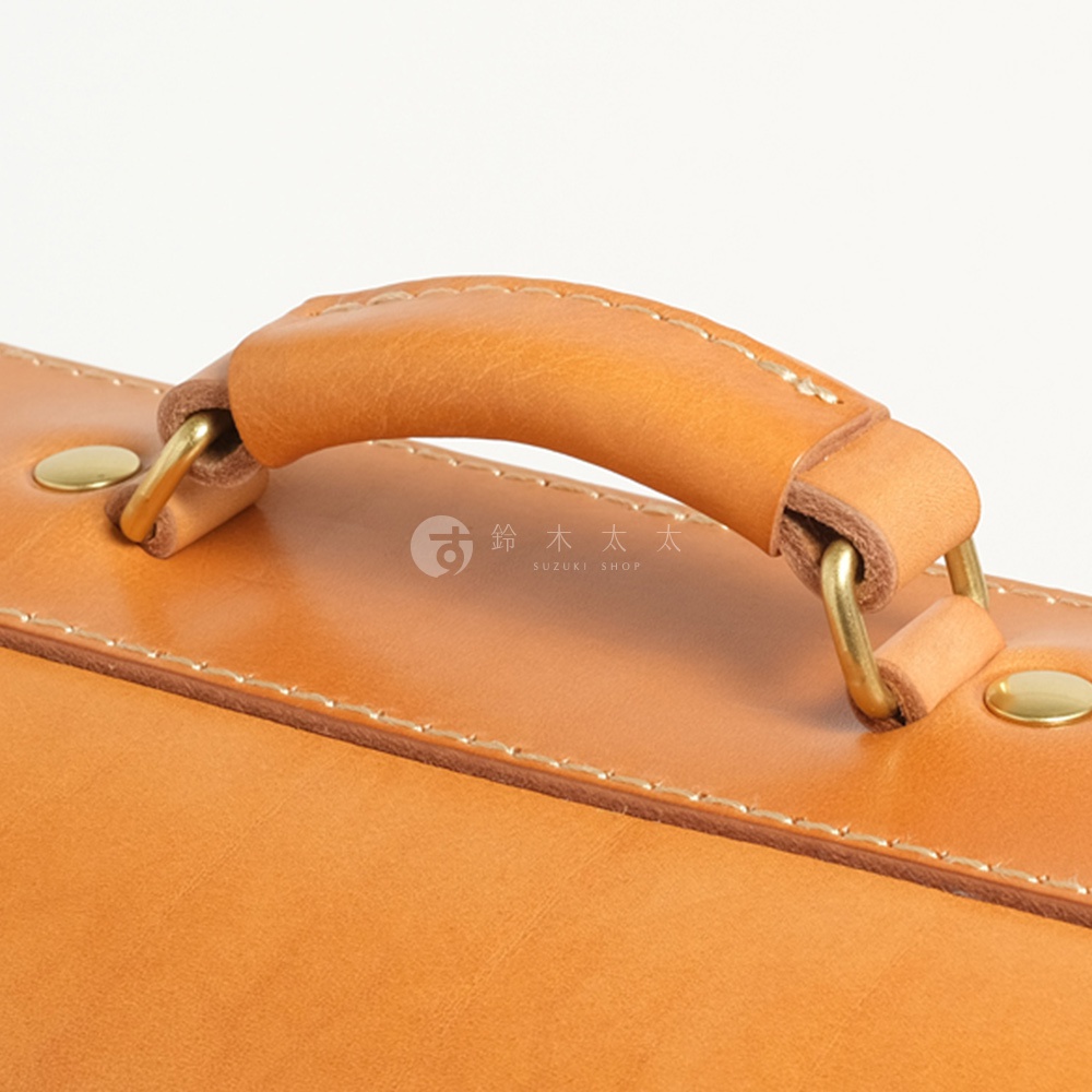 皮革手提包的特寫，展示了其圓潤的提把、金屬扣環和精緻的縫線細節