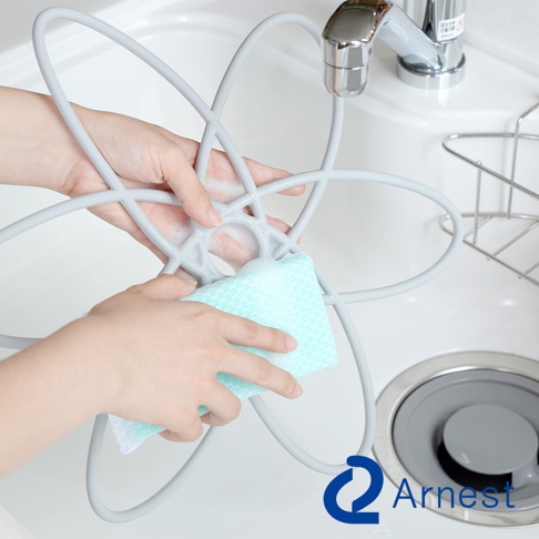 一雙手正在清潔一個灰色、扇形設計的鍋具防刮保護墊，墊上有泡沫，旁邊是水槽和水龍頭。