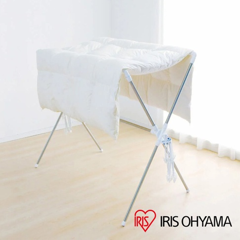 銀色不鏽鋼X型曬衣架，支架上鋪著白色羽絨被，整體為簡易組裝設計。