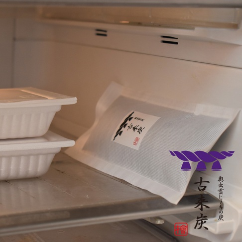 白色無紡布包裝的細長型木炭，內部填充黑色木炭顆粒，包裝上印有日文標籤和紫色的繩結圖案，產品旁邊堆疊兩個白色帶蓋的容器。