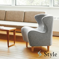 灰色布藝美姿調整座椅，椅背呈流線型，搭配木質椅腳，置於淺色沙發與木桌旁。