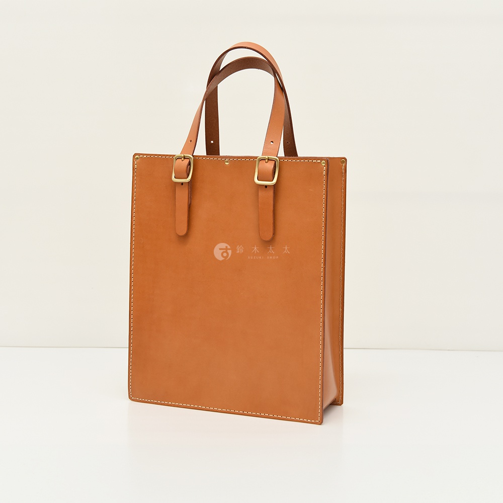 職人手作皮革商務用紙袋托特包，焦糖棕色，方正造型，附有兩條皮革提把及可調節的銅色金屬扣環，包身有細緻的縫線裝飾，中央印有品牌Logo。