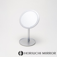 銀色金屬材質的桌上型化妝鏡，圓形鏡面周圍帶有LED燈，鏡面下方有四個圓形觸控按鈕。鏡子由一支細長的圓柱形支架連接至圓形底座。