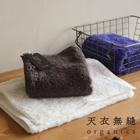 三條蓬柔長纖匹馬棉毛巾，顏色為深棕色、白色和藍色。深棕色毛巾上有品牌標籤，白色毛巾鋪在下方，藍色毛巾則放在金屬籃中。