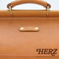 職人手作皮革旅行包 A-102，採用天然皮革材質，呈現溫潤的棕褐色，配有堅固的提把與精緻的品牌烙印，展現日式細膩工藝。