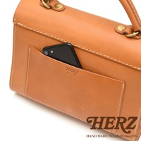 日本HERZ手工皮革單肩包，棕褐色皮革上有HERZ和made in Japan壓印，側邊插著一支手機